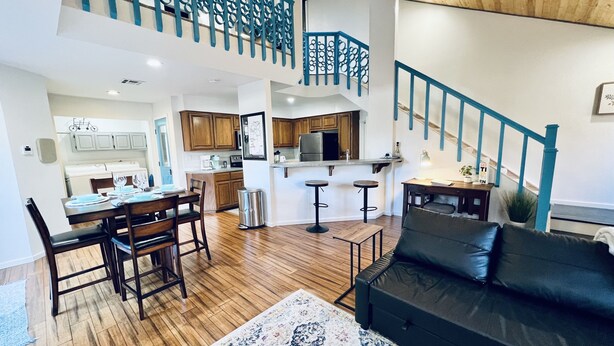 Amplia sala de estar con una mesa de comedor, sofá de cuero negro y una escalera con barandales azules.