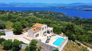 Une villa moderne dotée d’une piscine, entourée d’une végétation luxuriante et offrant une vue sur une vaste étendue d’eau.