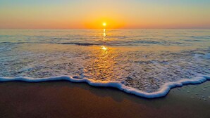 Ein Strand bei Sonnenuntergang, sanfte Wellen spiegeln sich im Ufer wider.