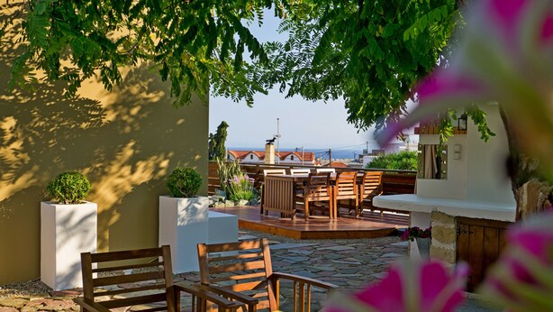 Eine Terrasse im Freien mit Holzmöbeln, einem Grillbereich und Blick auf das Meer.
