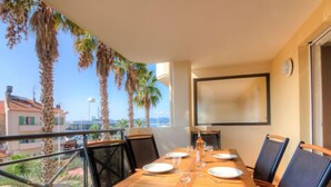 Zona pranzo con tavolo in legno apparecchiato per sei, con vista su un balcone con palme e sullo skyline della città.