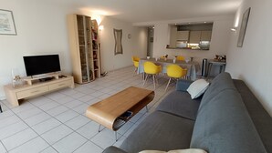 Un soggiorno moderno con un divano grigio, un tavolino in legno, una televisione e una zona pranzo con sedie gialle e un tavolo.