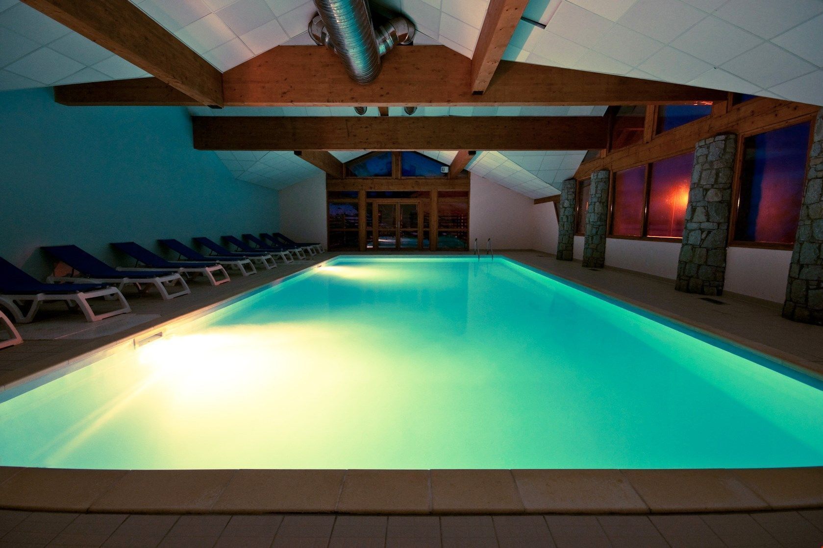 Ein Innenpool mit Holzbalken, Steinpfeilern und Liegestühlen.