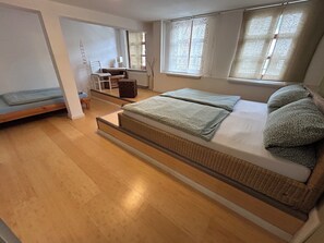 Ein Zimmer mit einem Bett, einem Sessel, einem kleinen Tisch und einem Fenster.