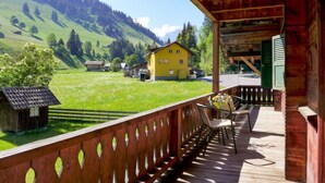 A wooden deck with a view of a green valley and a yellow house. - Chalet Alte Post by Interhome (Schwenden)