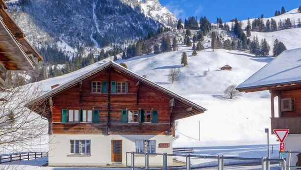 A wooden chalet with a sloped roof, a white exterior, and green shutters, set against a backdrop of snow-covered mountains and a clear blue sky. - Chalet Alte Post by Interhome (Schwenden)