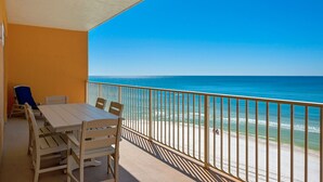 Een balkon met een houten tafel en stoelen, met uitzicht op een strand en een helderblauwe lucht.