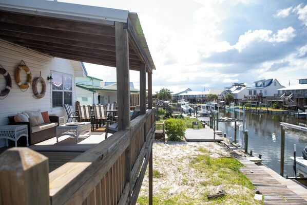 A wooden deck with outdoor furniture, a covered area with a railing, and a view of a marina with boats docked.