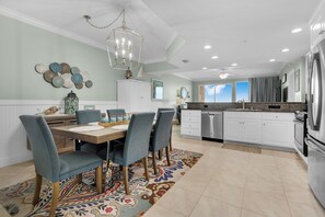 A modern kitchen with white cabinets, stainless steel appliances, and a dining area with a wooden table and blue chairs.