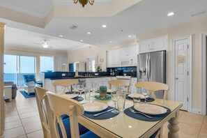 A modern kitchen with white cabinets, a stainless steel refrigerator, and a dining area with a glass table and blue chairs.
