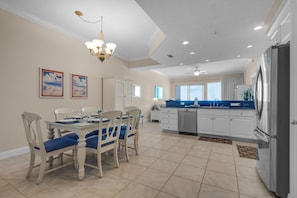 A spacious kitchen with white cabinetry, a stainless steel refrigerator, and a dining area with a glass table and white chairs.