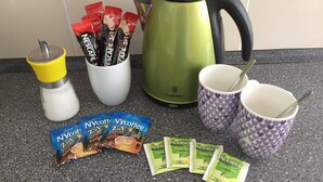 A kitchen counter with a kettle, coffee maker, cups, and coffee packets.