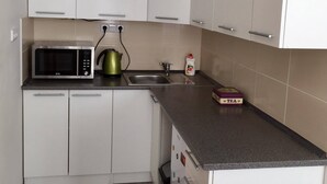 A kitchen with white cabinets, a microwave, a kettle, a sink, and a tea box.