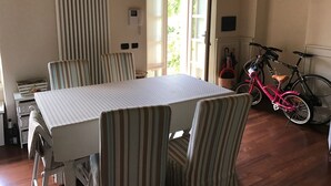 A dining area with a table and chairs, a radiator, a window with curtains, and a bicycle. - Historic residence La Quassa Ispra Lake Maggiore (Ispra)
