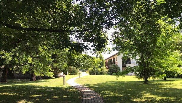 A paved pathway leading to a building with arched windows, surrounded by lush green trees and grass. - Historic residence La Quassa Ispra Lake Maggiore (Ispra)