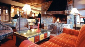 A cozy lounge area with plaid sofas, a glass-top coffee table, and a stone fireplace. - Appartement avec balcon/terrasse | Accès piscine (Aime)