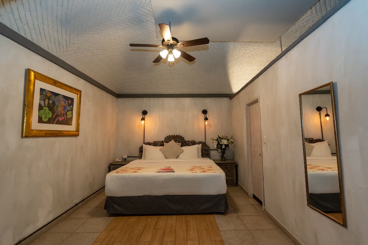 A bedroom with a bed, a ceiling fan, a nightstand, a mirror, and a framed picture on the wall.
