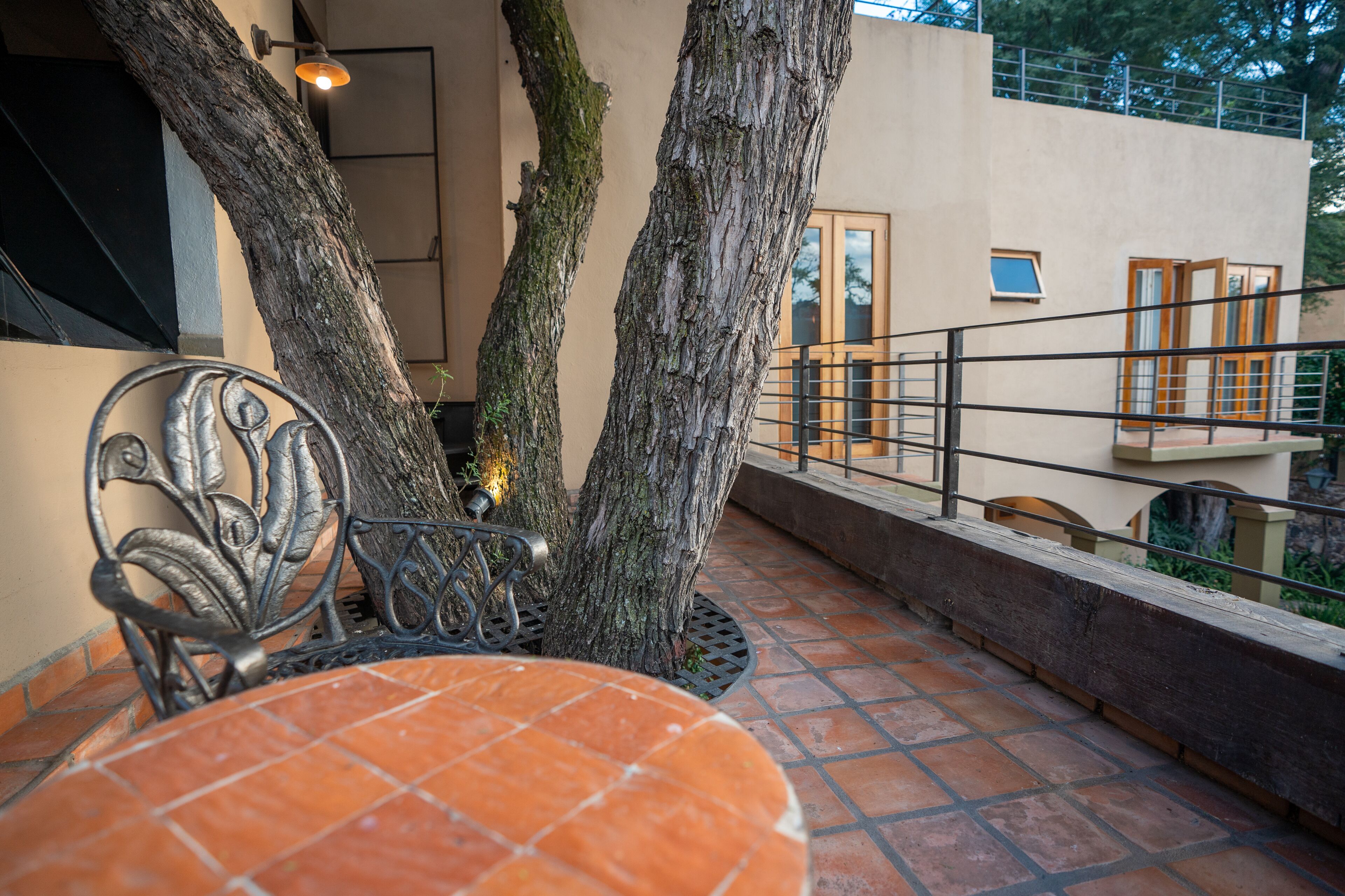 Una terraza con mesa y sillas, rodeada de árboles y una barandilla.