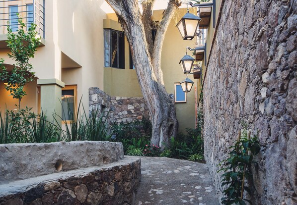 Um beco estreito com uma parede de pedra, uma árvore e um edifício com varanda.