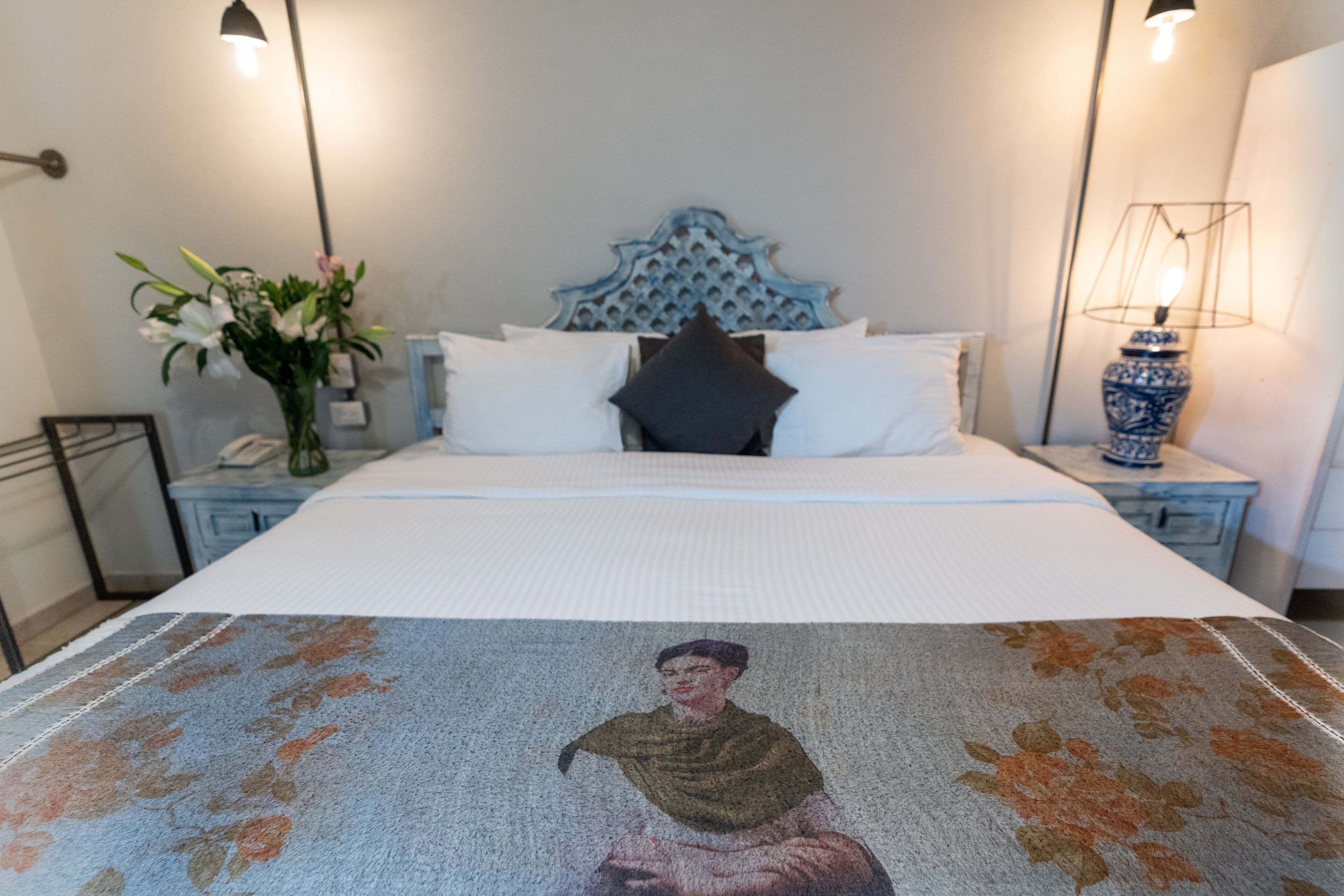 A bedroom with a bed, a nightstand, a lamp, and a vase with flowers.