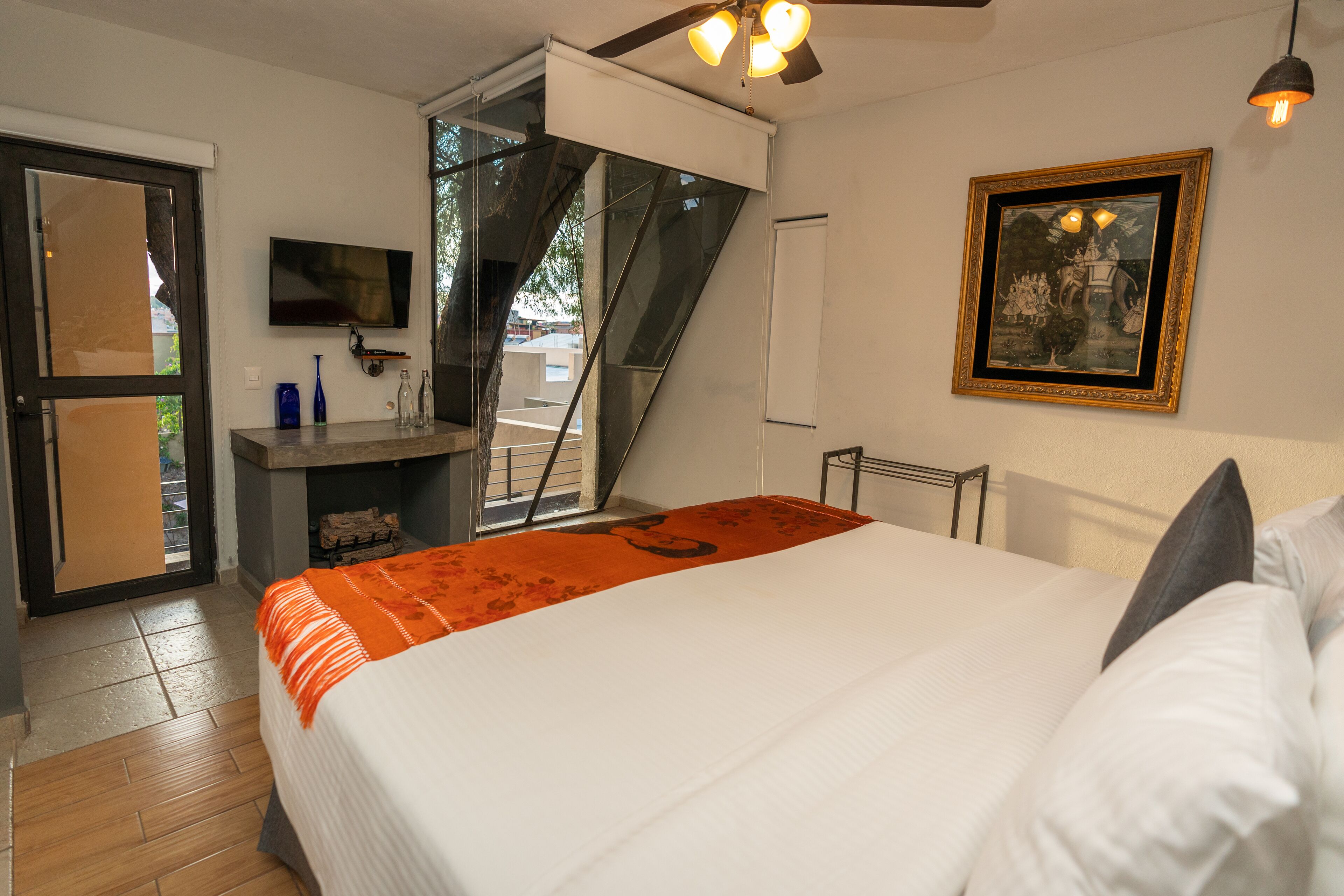 Un dormitorio con una cama, un televisor, un cuadro y una escalera que lleva a un balcón.