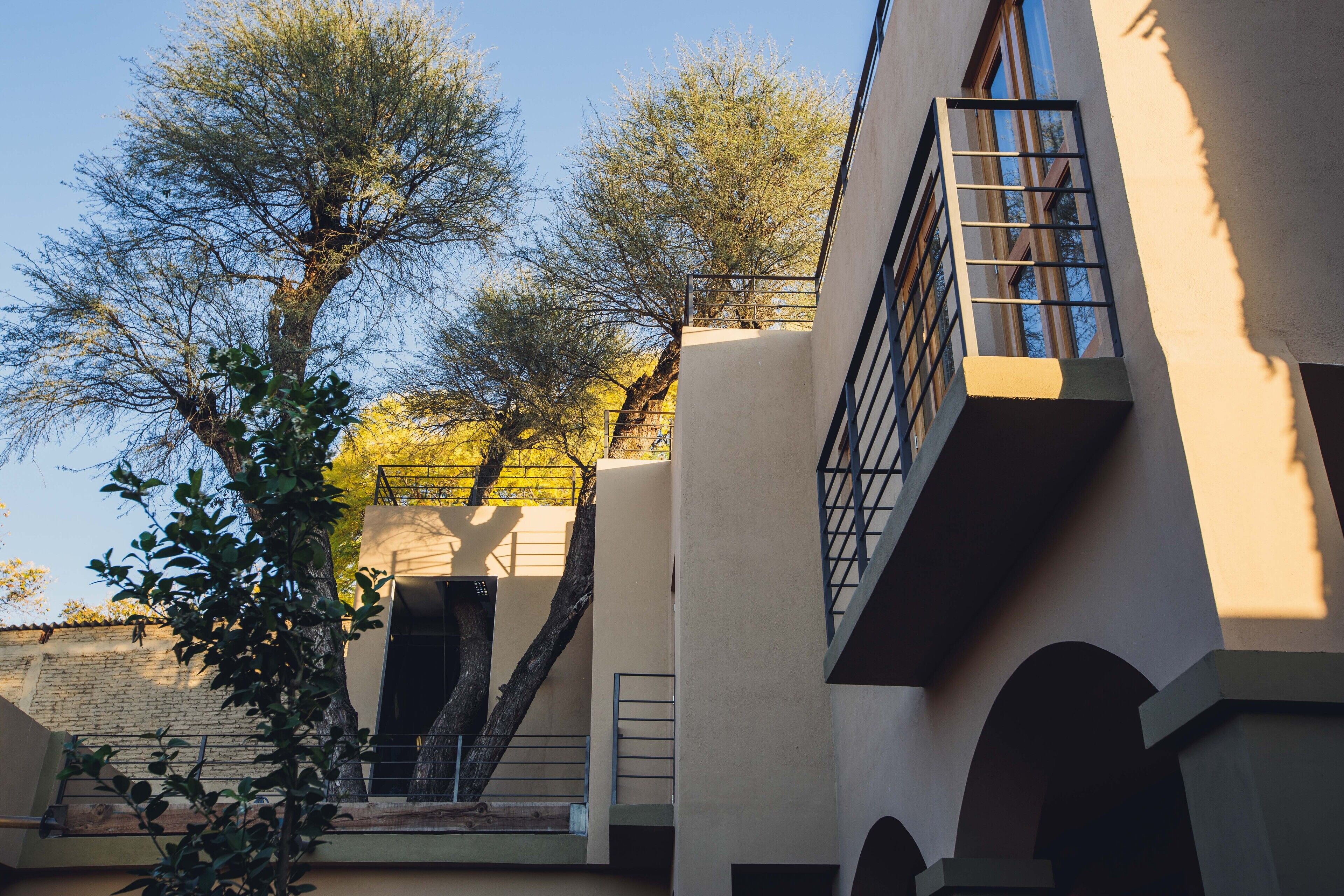 A building with a modern architectural style, featuring a staircase leading to an upper level, a balcony with a metal railing, and a tree in the foreground.