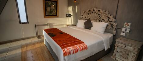 A bedroom with a large bed, a painting on the wall, a ceiling fan, and a nightstand with a lamp.