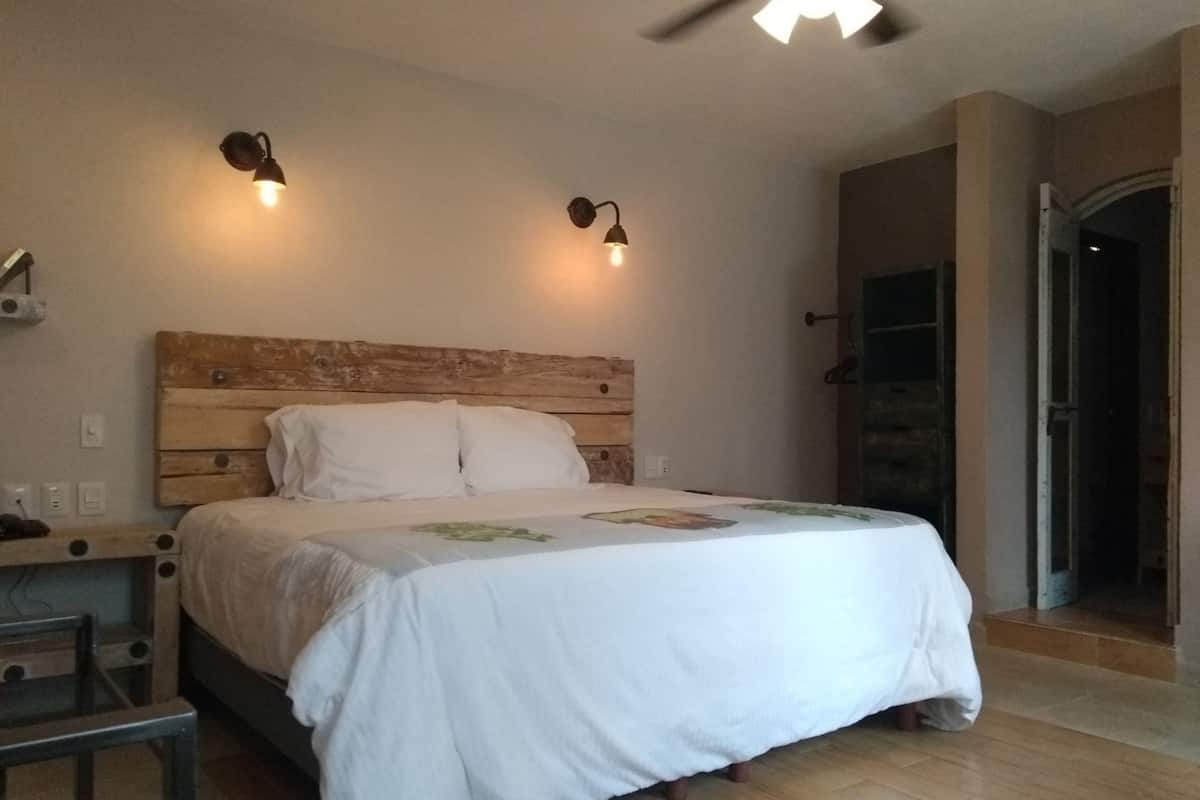 A bedroom with a wooden headboard, two bedside lamps, a bed with a white bedspread, a small table, and a chair.