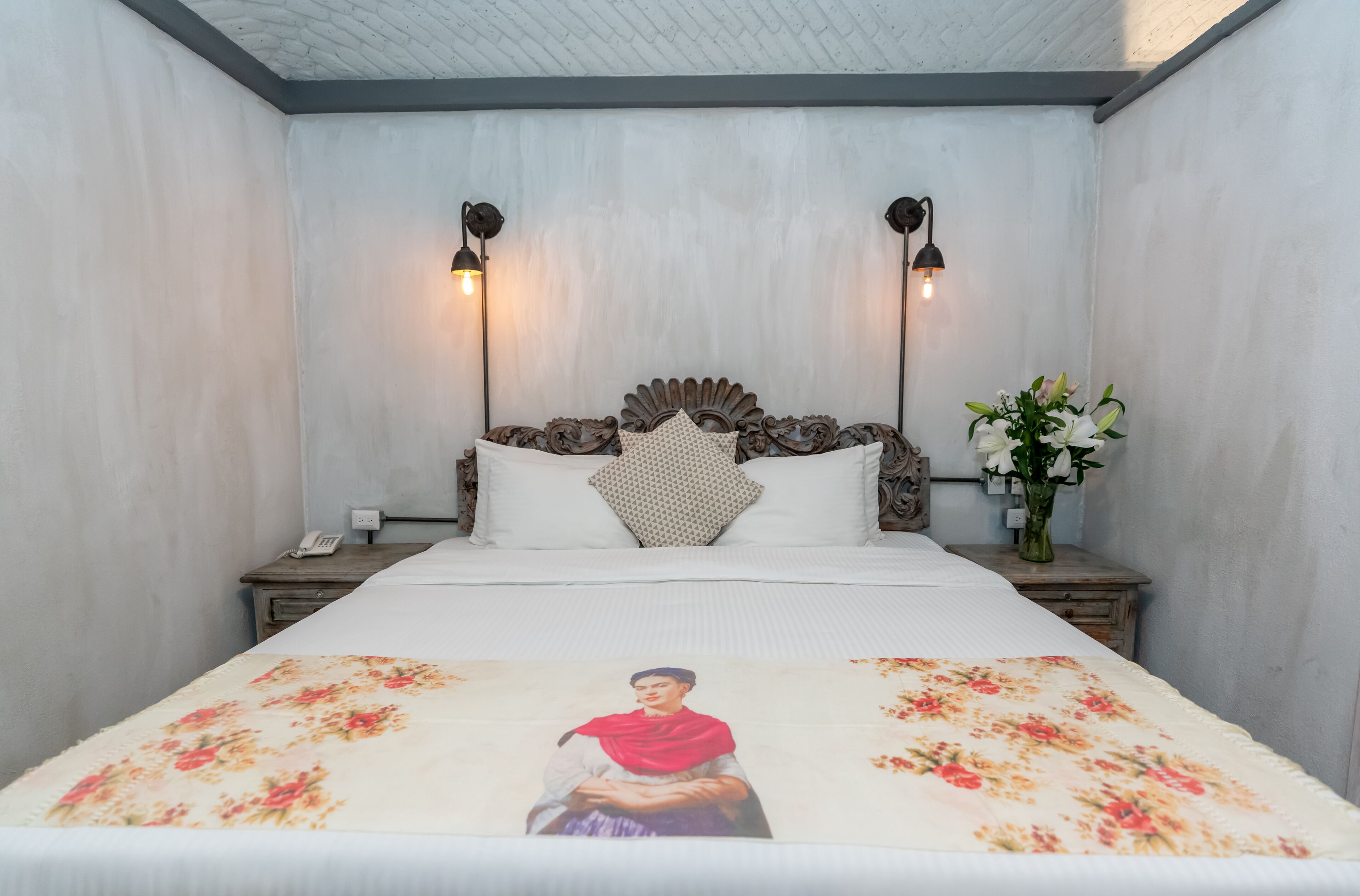 A neatly made bed with a floral bedspread, a decorative headboard, and two bedside lamps.