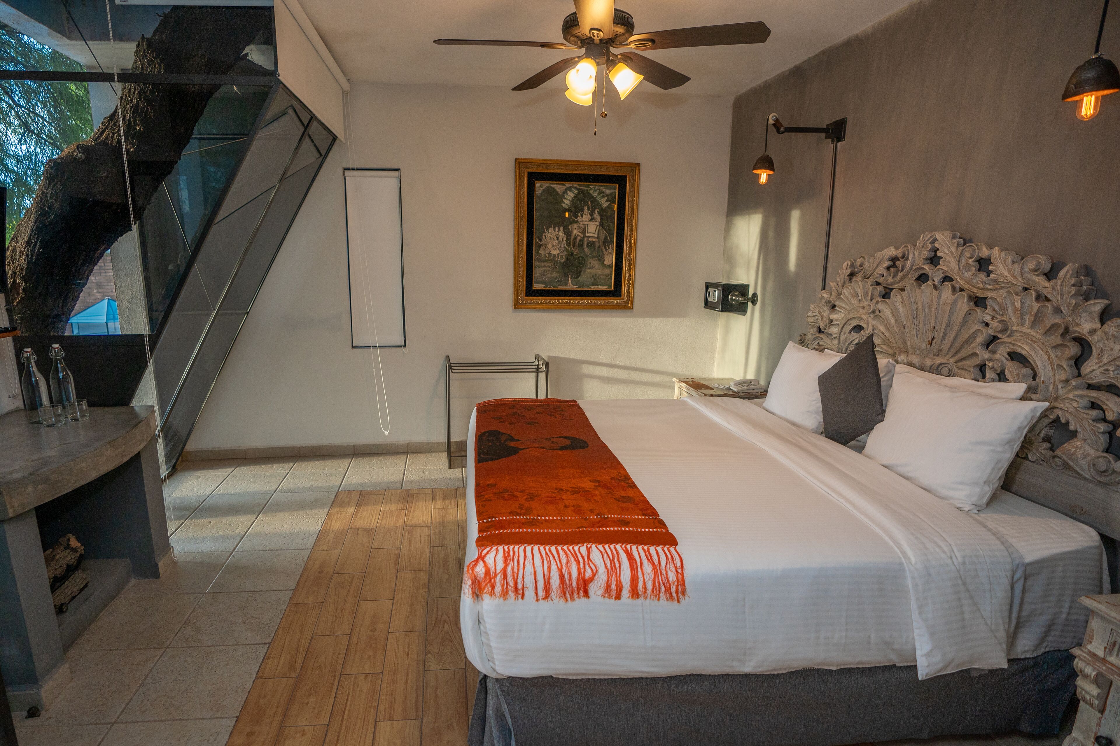 A bedroom with a large bed, a ceiling fan, a framed picture on the wall, and a staircase.