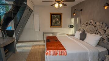 A bedroom with a large bed, a ceiling fan, a framed picture on the wall, and a staircase.