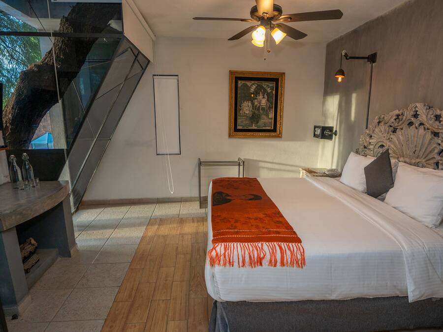 A bedroom with a large bed, a ceiling fan, a framed picture on the wall, and a staircase.