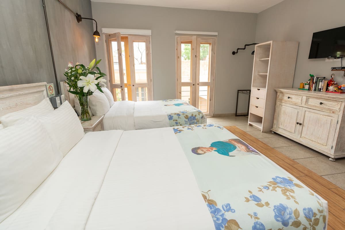 A hotel room with two beds, a wooden floor, a white dresser, a television on the wall, and a door leading outside.