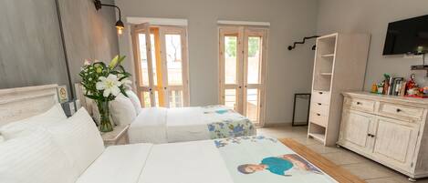 A hotel room with two beds, a wooden floor, a white dresser, a television on the wall, and a door leading outside.