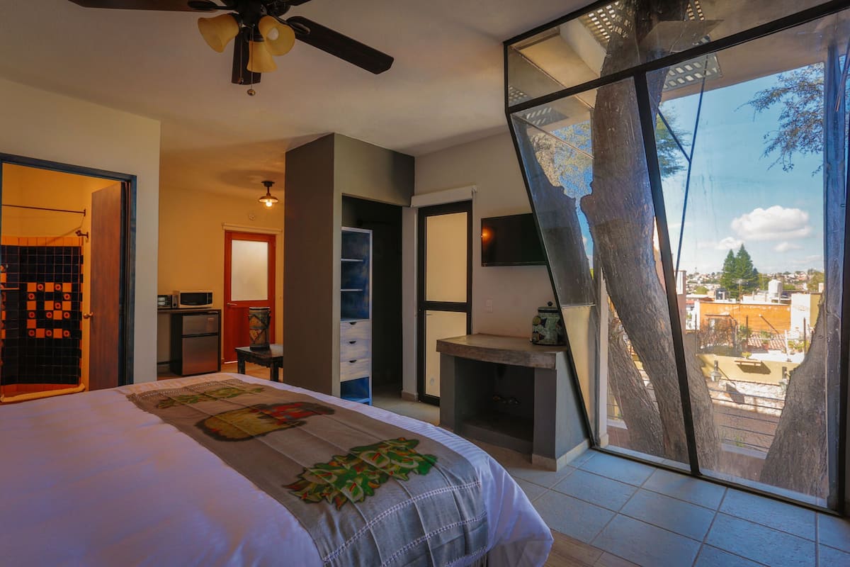 A bedroom with a bed, a ceiling fan, a TV, and a view of the outside.