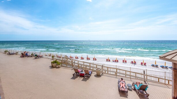 Blick auf einen Strand mit gepflastertem Weg, Liegestühlen und Sonnenschirmen.