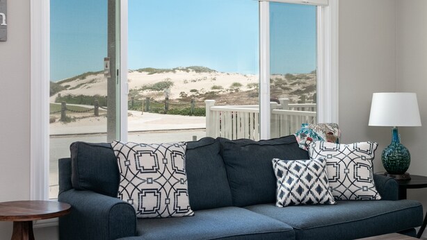 A living room with a large window offering a view of a sandy beach and dunes. - 1417G - "After Dune Delight" (Ventura)