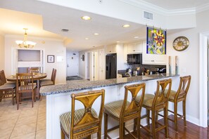 A modern kitchen with a central island, bar stools, and a dining area with a chandelier.