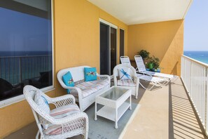 A balcony with wicker furniture, a glass table, and a view of the ocean.