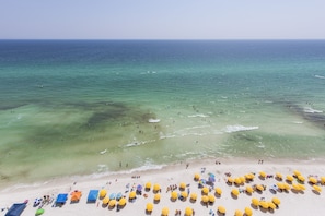 Een strand met helder turquoise water, mensen die zwemmen en veel gele parasols in het zand.