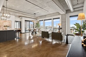 A spacious, modern interior with a kitchen area, dining space, and large windows offering city views.