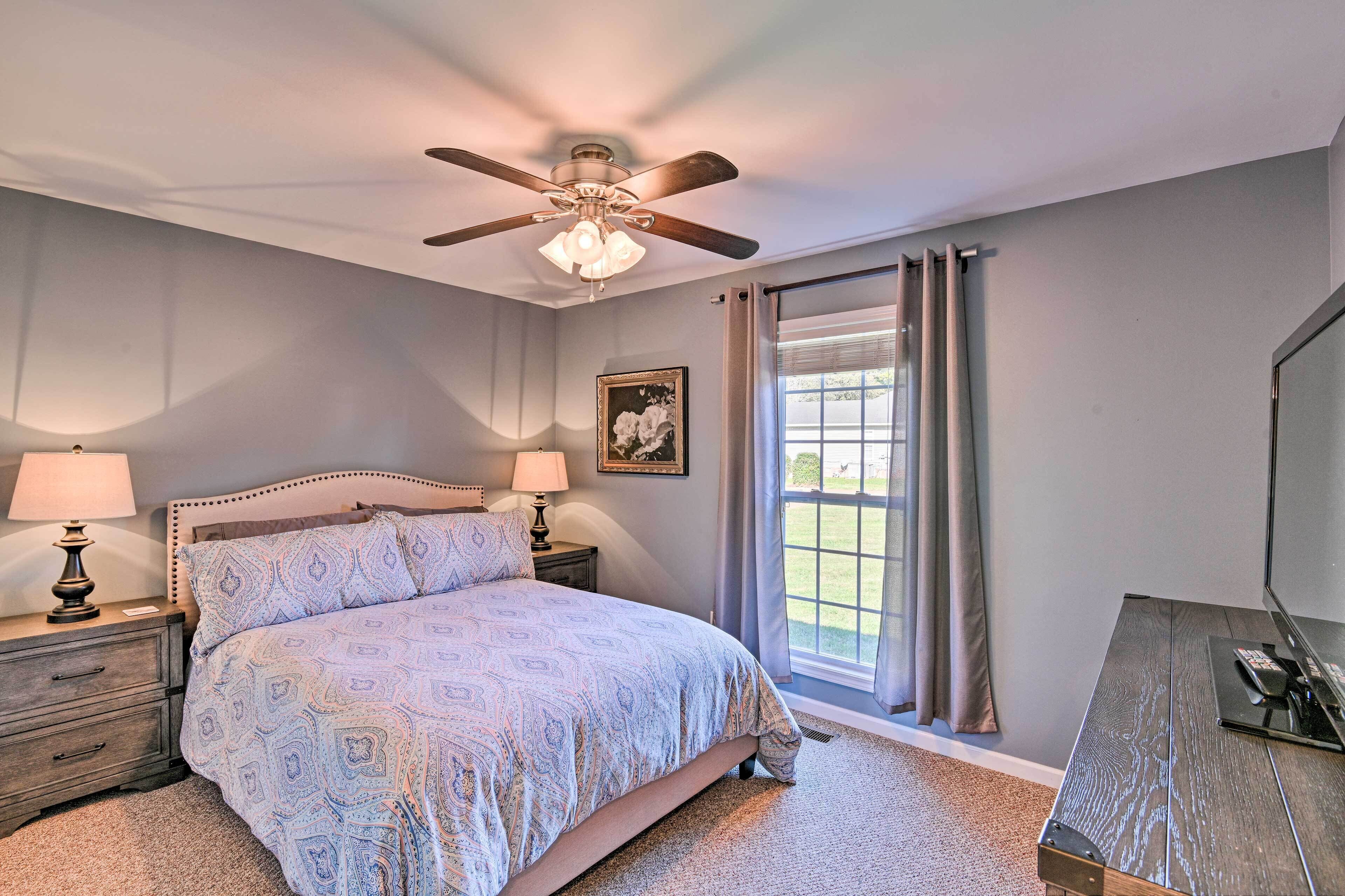 A bedroom with a bed, nightstands, a ceiling fan, a window with curtains, and a desk with a computer.