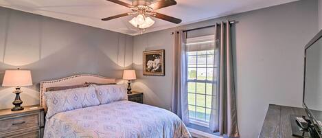 A bedroom with a bed, nightstands, a ceiling fan, a window with curtains, and a desk with a computer.
