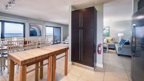 Une cuisine moderne avec une table à manger en bois, des meubles de rangement sombres et une vue sur l’océan.