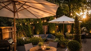 Une terrasse extérieure avec une table ronde en bois, des chaises, un barbecue et des parasols.
