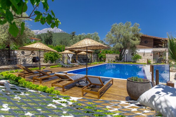 A poolside area with lounge chairs and umbrellas, a stone wall, and a view of the mountains.