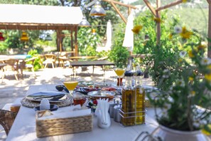 An outdoor dining area with tables set for a meal, surrounded by greenery and potted plants.