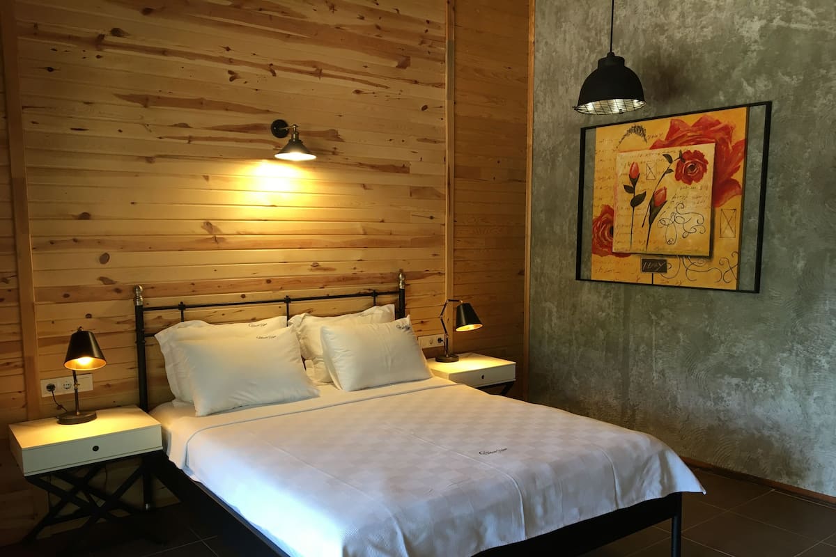 Ein Schlafzimmer mit einem hölzernen Kopfteil, zwei Nachttischlampen, einem Bett mit weißer Bettwäsche und einem gerahmten Kunstwerk an der Wand.