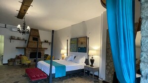Een slaapkamer met een stenen vloer, een bed met een witte spreidek, een rode bank, een houten stoel en een kroonluchter.