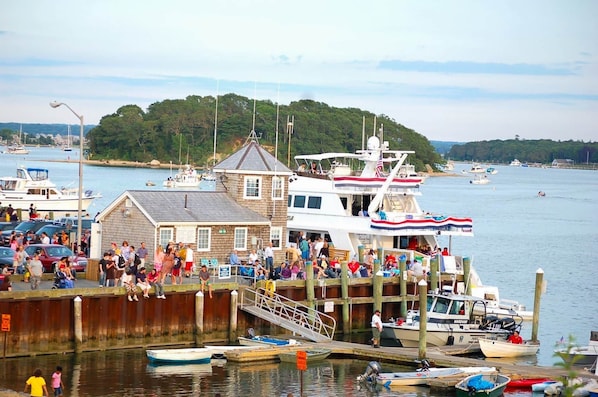 A docked boat with a crowd of people, a small building, and a forested hill in the background.
